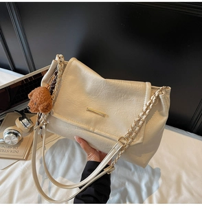 Detail of cream chain underarm bag with gold rectangle clasp and teddy bear charm