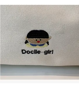 Detail of embroidered cartoon girl and Docile girl text on off-white canvas tote bag