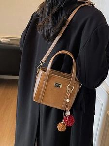 Brown faux suede bucket bag with plush pompom charm and metallic logo on textured leather