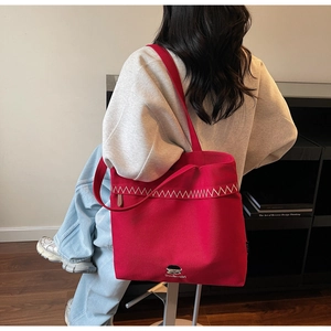 Close-up of red canvas tote bag with white wavy stitching and minimalist logo