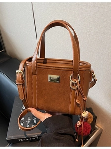 Brown faux suede bucket bag with leather handles and decorative tassel ornament