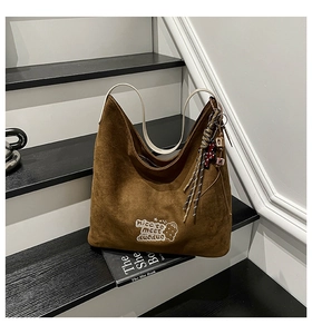 Detail view of brown suede hobo bag with white embroidery and decorative charms
