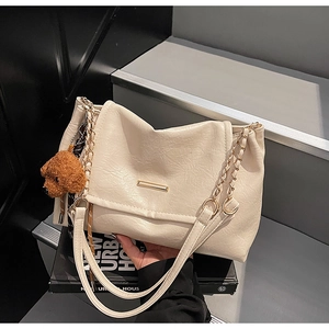 Detail of cream pleated shoulder bag featuring gold chain strap and cute bear charm