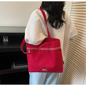Close-up of red canvas tote bag showing white zigzag stitching and cartoon logo detail