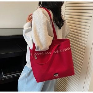 Detail view of red canvas tote bag with white zigzag embroidery and long shoulder strap
