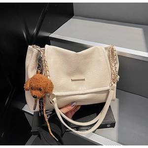 Close-up of cream PU leather shoulder bag with gold hardware and a teddy bear charm