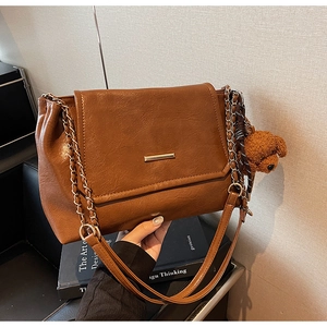 Detail of dark brown pebble leather bag with gold chain strap and cute bear charm