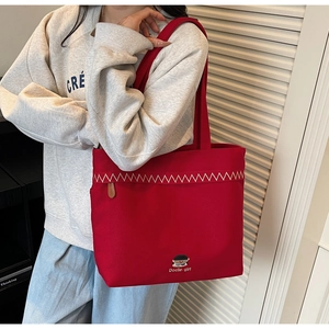 Model showcasing a large red canvas tote bag with white embroidery and cartoon patch