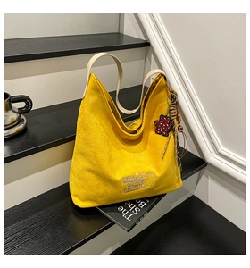 Detail of yellow suede tote bag with white embroidery and a cute red bear keychain