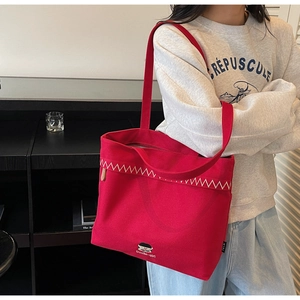 Detail view of red canvas tote bag featuring white zigzag embroidery and a cartoon patch