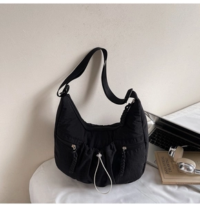 Close-up of black pleated crescent bag with multiple zip pockets and white drawstring details