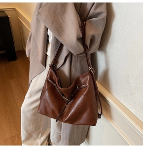 Detail view of large brown leather tote bag with side drawstring worn with suit