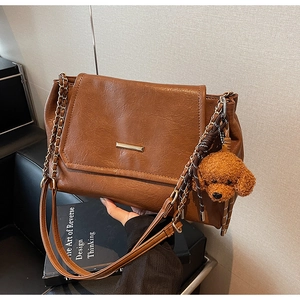 Detail of brown vintage leather shoulder bag with golden bar and cute poodle charm accessory