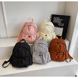 Five small nylon backpacks in pink, beige, black, grey and brown on white steps