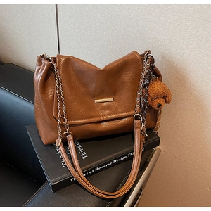 Detail of caramel oil-wax leather shoulder bag with gold metal bar and teddy bear charm