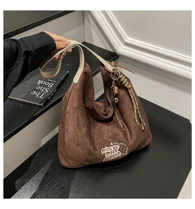 Detail of dark brown suede hobo bag with teddy bear embroidery and braided strap