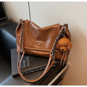Detail of a brown PU leather shoulder bag featuring a cute plush dog charm and chain strap