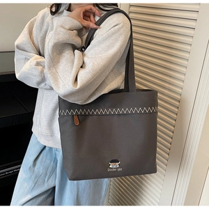 Detail of dark grey canvas tote bag with white wavy embroidery and cute girl logo
