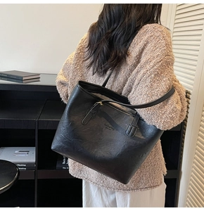Detail view of large black leather tote bag with fashion bag lettering worn by model