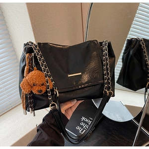 Detail of black faux leather tote with gold chain strap and cute brown plush puppy charm