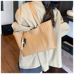 Detail view of woven brown tote bag with decorative beads worn with a beige trench coat