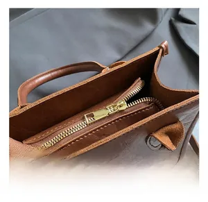 Close-up of golden zipper hardware on brown leather vintage handbag with smooth texture