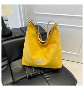 Detail of yellow tote bag with bear embroidery and white leather handles on a sofa