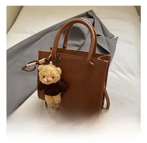 Detail of vintage brown tote bag with bear charm on a grey blazer and book