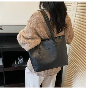 Detail of a large black crinkled leather tote bag worn by a model in a stylish room