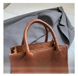 Close-up of brown leather handbag handle with detailed stitching and lychee grain texture