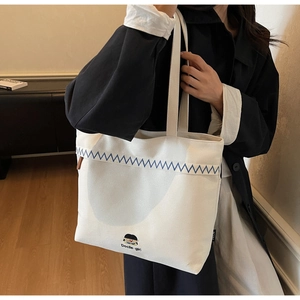 Detail of white canvas tote bag featuring blue embroidery and cute cartoon girl graphic