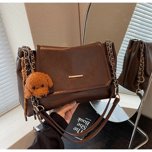 Detailed shot of coffee brown vintage shoulder bag with golden buckle and teddy pendant