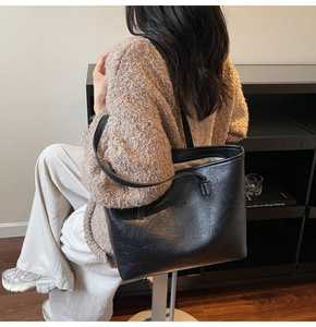 Black tote bag with textured finish and NEW YORK text worn by a model in a cozy room