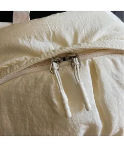 Detail of double zipper with extended white cord pulls on a cream-colored textured backpack