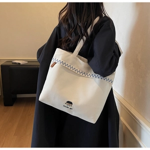 Detail of off-white canvas tote featuring blue zigzag stitching and cute girl embroidery