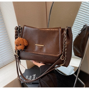 Detail of dark brown wax leather bag with metal chain strap and cute teddy bear pendant