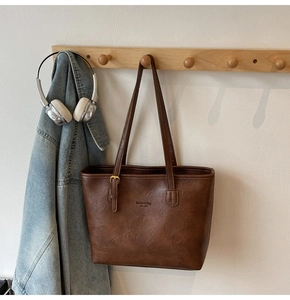 Detail of dark brown faux leather tote bag with New York text on a wooden wall hook