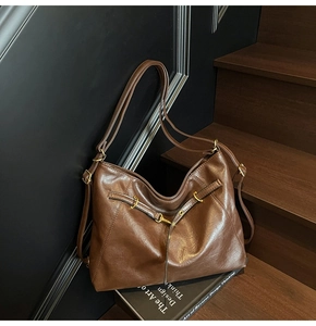 Detail view of large dark brown tote bag with vintage metal buckles on a black book