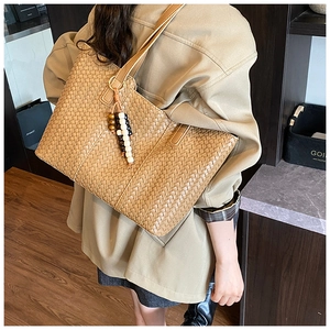 Detail of a large brown woven leather tote bag with a three-color beaded tassel pendant