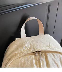 Detail of cream white lightweight backpack featuring webbed handle and dual zipper closure