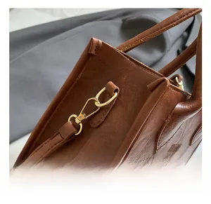 Detail of vintage brown leather bag with golden metal hook and embossed brand lettering