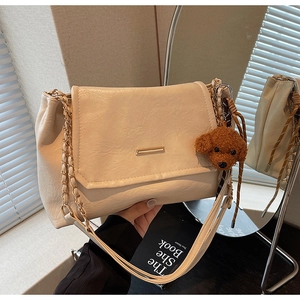 Detail of cream chain shoulder bag featuring soft pleated texture and plush teddy charm