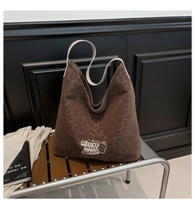 Detail view of large leopard print tote bag with bear embroidery on dark wooden bench
