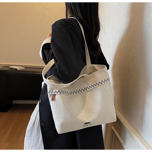 Detail of off-white canvas tote bag featuring navy zigzag embroidery and logo print
