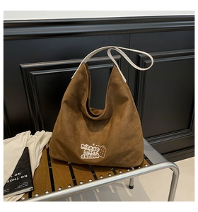 Detail of caramel suede tote bag with white embroidery and cute cartoon pattern on a bench