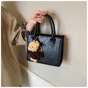 Close-up of black pleated leather tote bag featuring a cute teddy bear plush charm