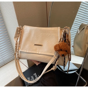 Close-up of beige pleated leather shoulder bag with gold chain and plush bear charm