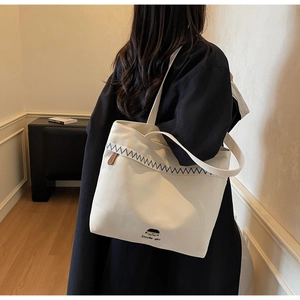 Detail of off-white canvas tote bag with Docile-girl print and blue zigzag stitching