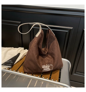 Detailed view of cartoon bear embroidery on brown suede tote bag with cream straps