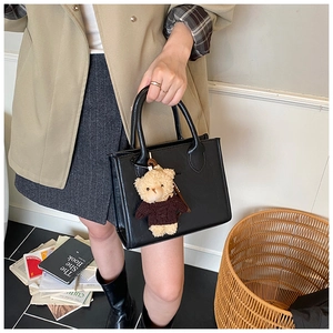 Detail of black tote bag with smooth texture and cute teddy bear plush charm